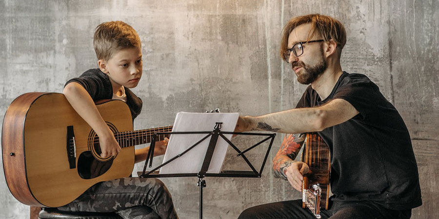 a man teaching a boy how to play guitar