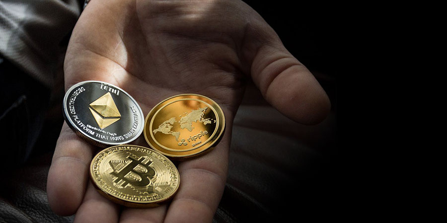 three crypto coins including a silver Ethereum on top of a person's palm